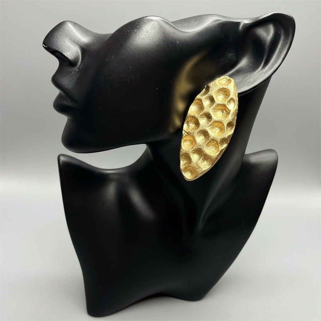 Gold textured earring on a black mannequin ear with a beige background