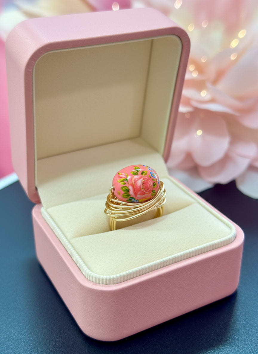 Pink ring box with a gold ring featuring a floral design on a soft pink background.
