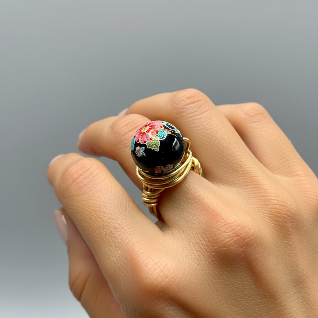 Gold ring with a floral design on a black background worn on a finger.