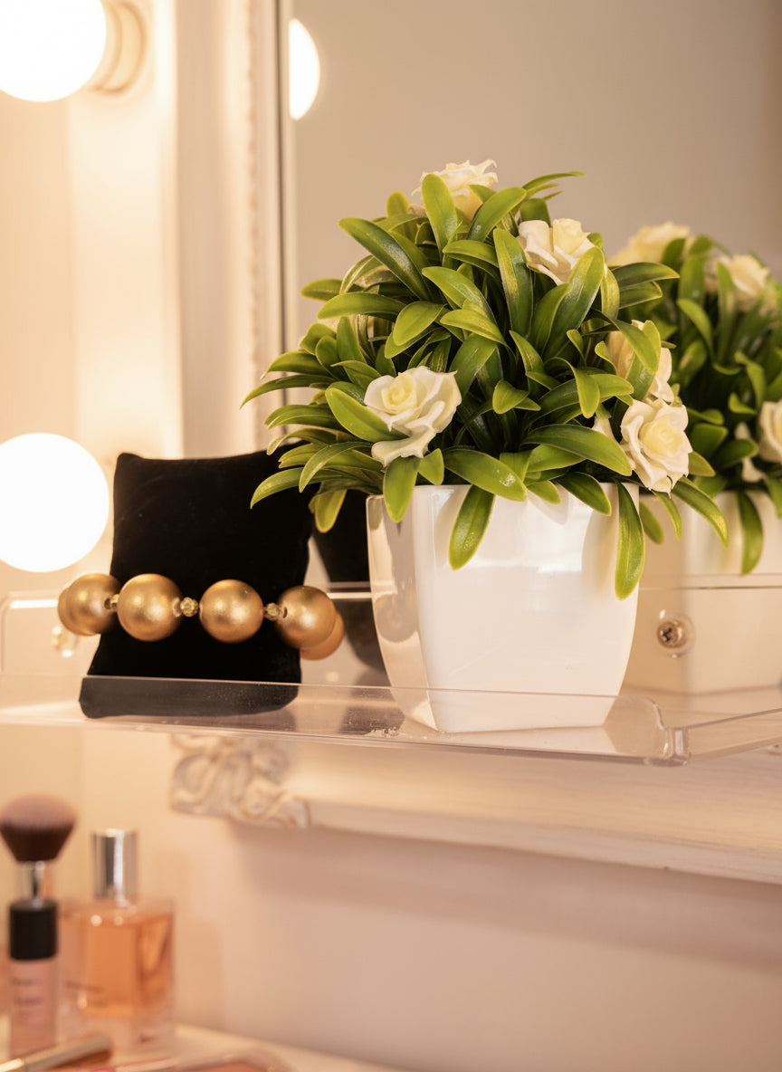 gold beaded stretch bracelet with Decorative wall planter with greenery and white flowers against a wall.