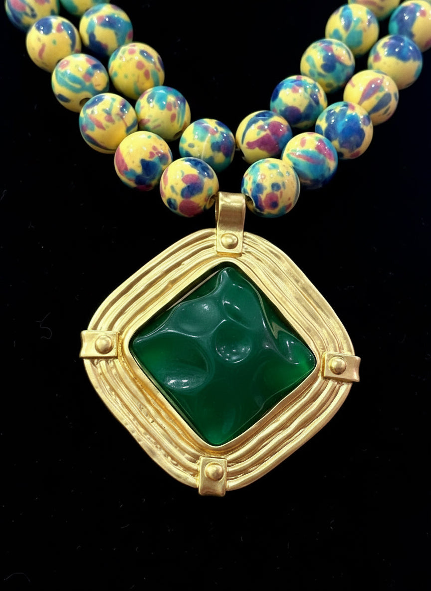 Gold pendant with green stone held by a hand against a dark background