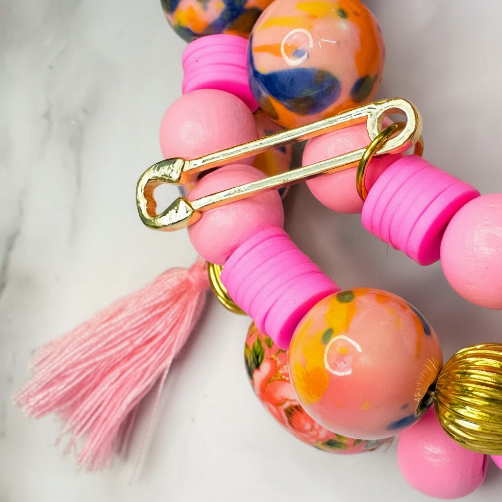 Beaded bracelet with pink tassel and gold safety pin on a marble surface